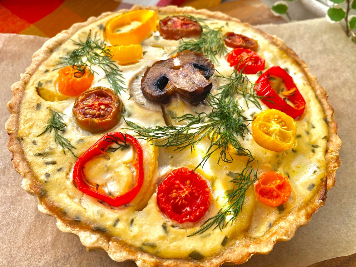 A whole vegan roasted veggie quiche on a wooden tray