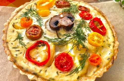 A whole vegan roasted veggie quiche on a wooden tray