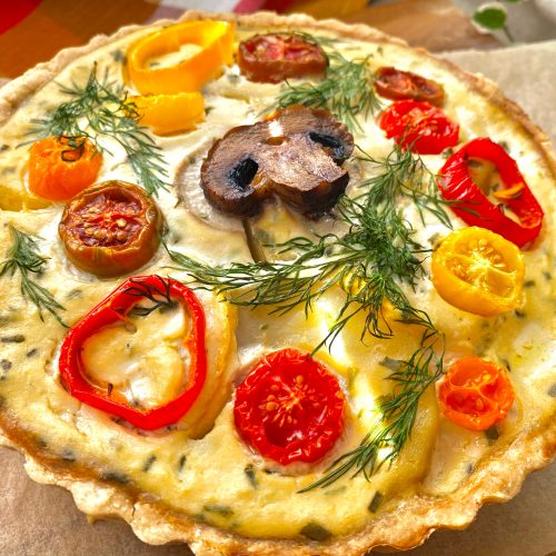 A whole vegan roasted veggie quiche on a wooden tray